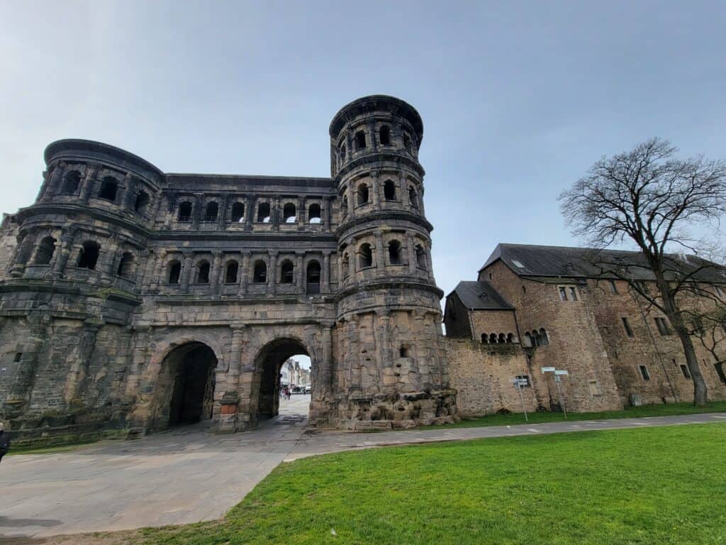 A large dark stone building with a rounded tower filled with windows over two arched passages