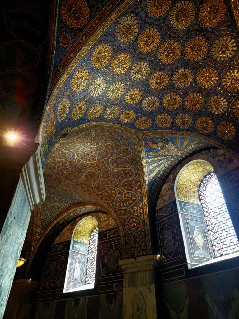 Two windows with leaded clear glass, and an arch overhead with blue and gold mosaics that look like sunflowers