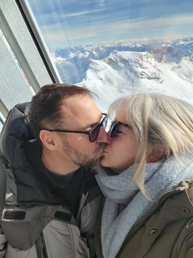 A man and woman kissing on the Zugspitze cable car with snowy mountains in the background