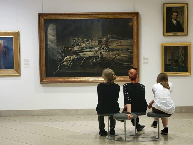 Three women sit on a bench looking at a painting in the National Museum in Poznań Poland