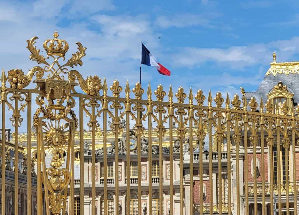 The French flag flies over the palace of Versailles as seen through the golden gate.