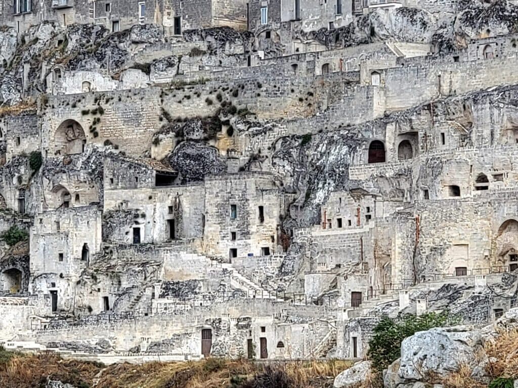 A solid cliff wall of residential buildings with cave-like older dwellings on the bottom, Medieval dwellings in the center layer and modern structures sitting on top.