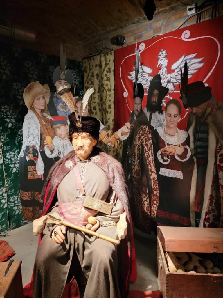 A figure of a man in rustic clothing sits next to a box of potatoes