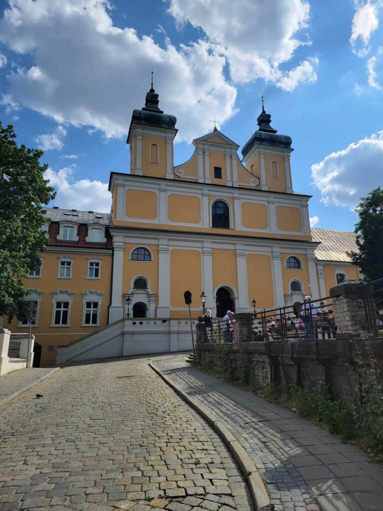 A yellow and white Baroque church with two black-capped towers