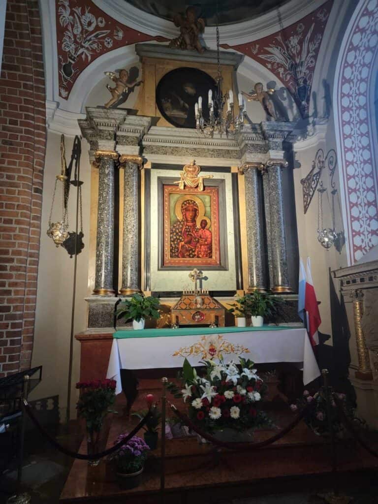 An altarpiece with a painting of a dark-skinned madonna and child, white flowers in front