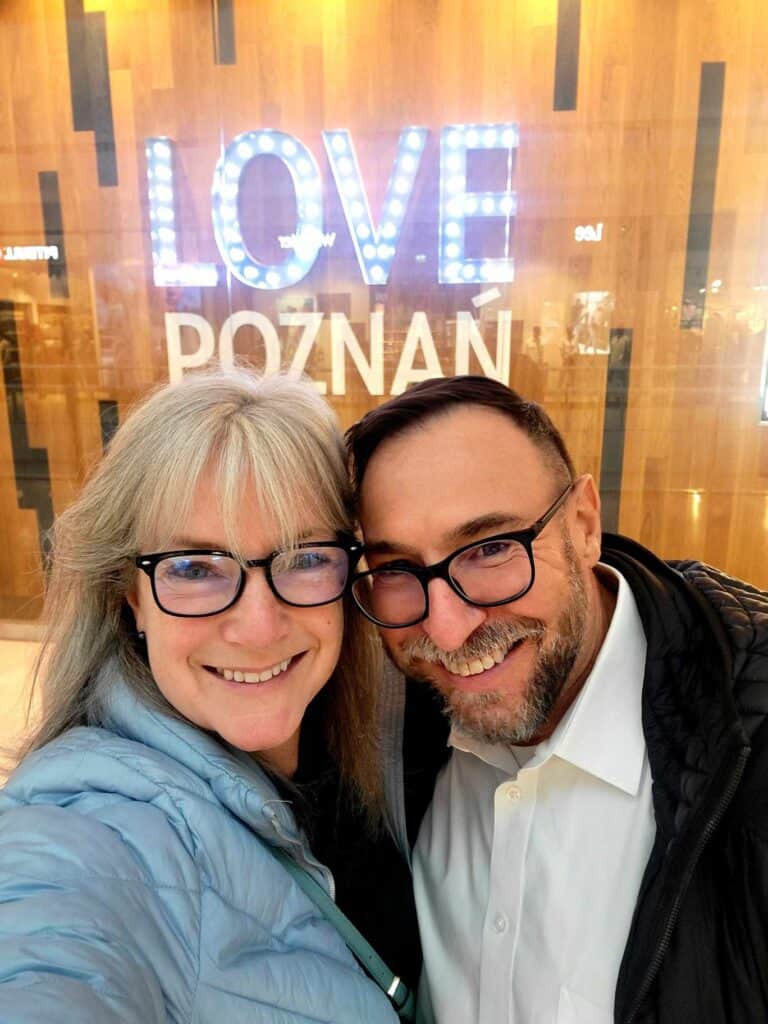 A smiling couple in front of an illuminated sign that reads "LOVE POZNAN"