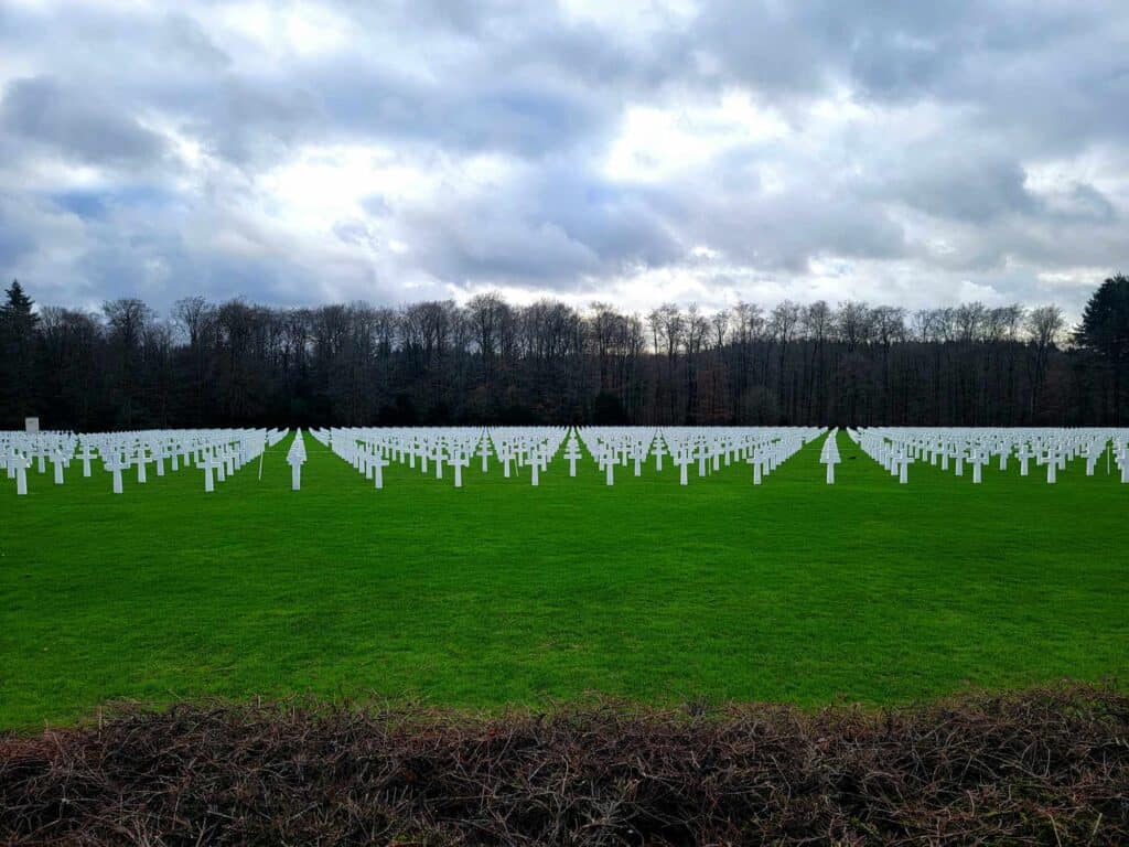 A green field with hundreds of white crosses and grave markers on a cloudy day