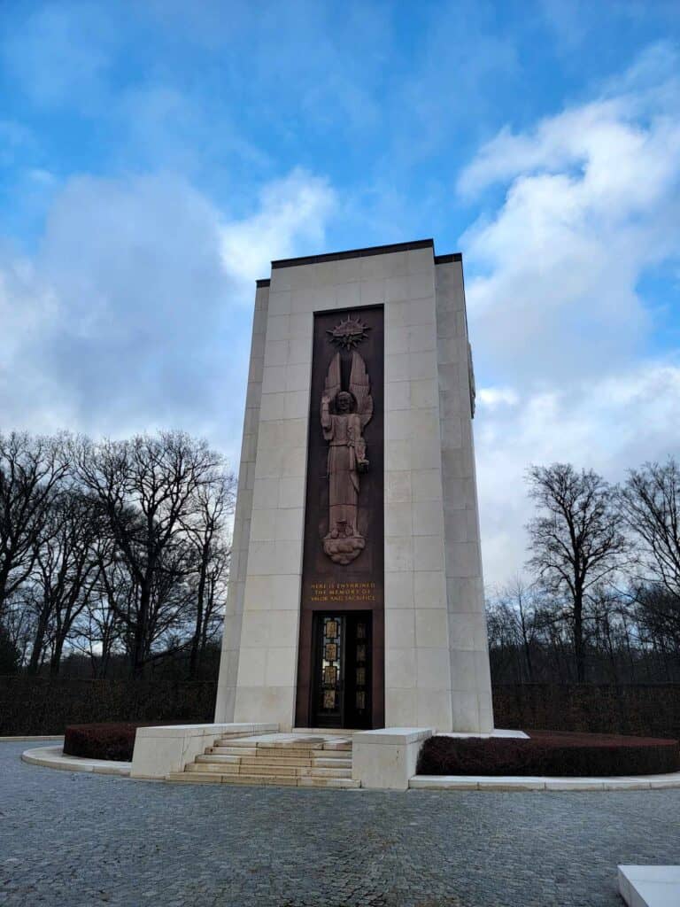 A tall pale stone monument with a darker panel over a door, featuring a winged standing angel