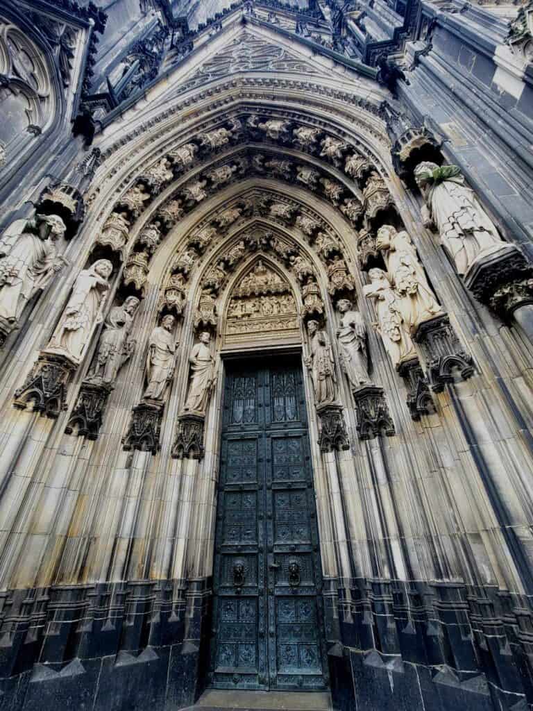 An ornate door of Cologne Cathedral with arched stonework and sculptures of the apostles