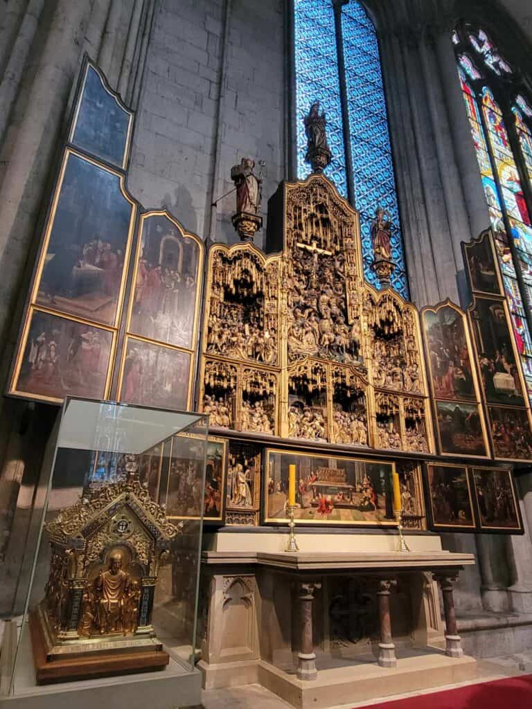 An ornate altarpiece with gold detail and frescoes on the side panels