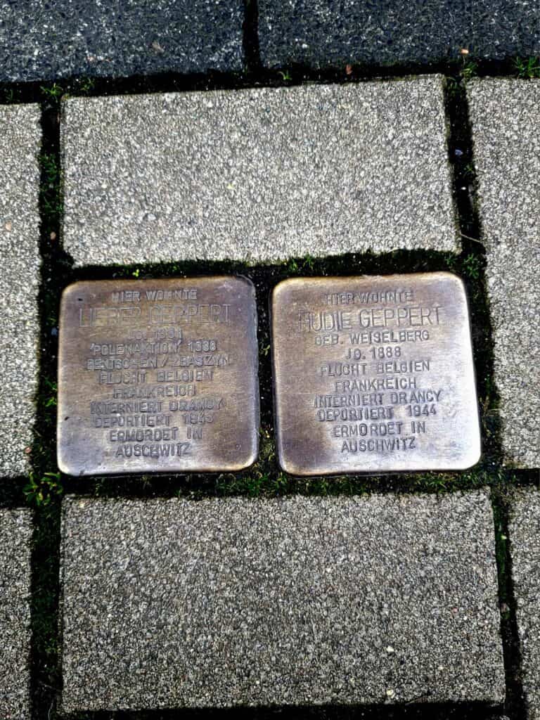 Two bronze plaques embedded in the sidewalk showing text in German explaining the fate of Lieber and Hudie Geppert.