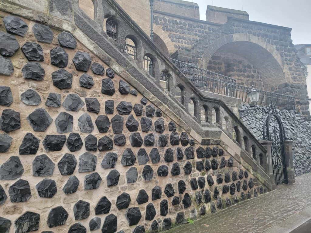 A wall with a stair railing in cement, on a wall made of black pentagonal stones with white mortar