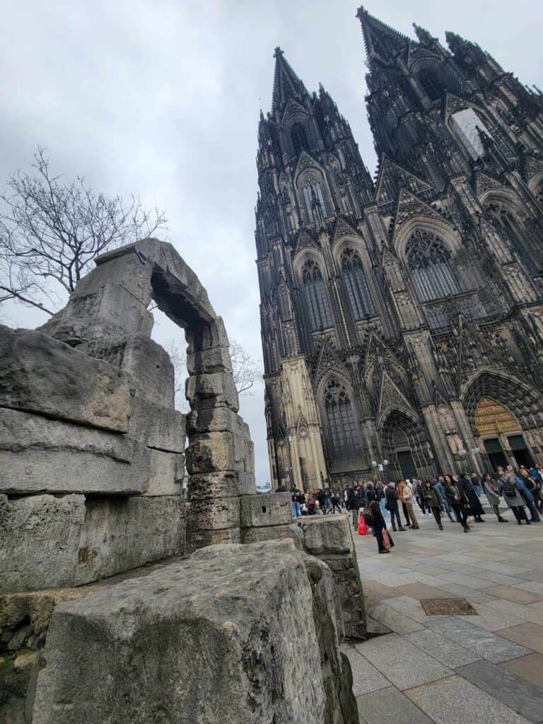 The double spires of Cologne Cathedral in the rear and an ancient roman arched gate in the forefront