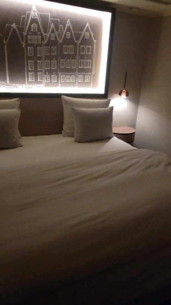 Large made bed with lighted art above in the Wasserturm Hilton Cologne