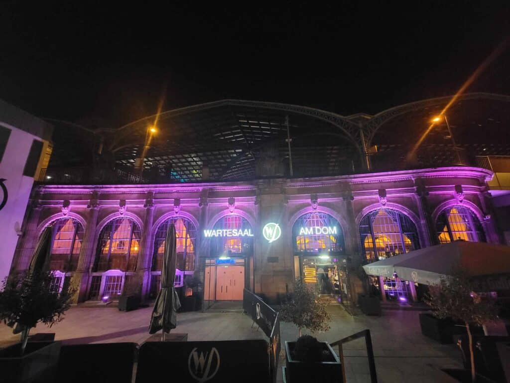 The outside of Wartesaal am Dom restaurant  with multiple windowed arches lit up in purple and pink lights