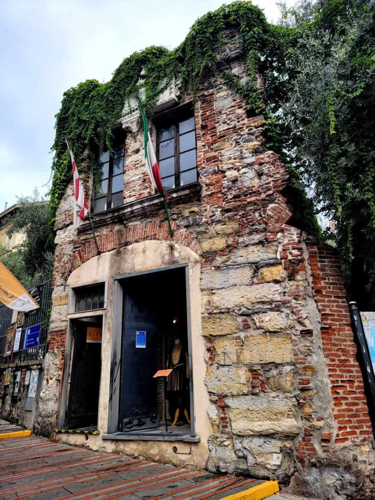 A small two story stone house with a large window and door and the flag of Italy 