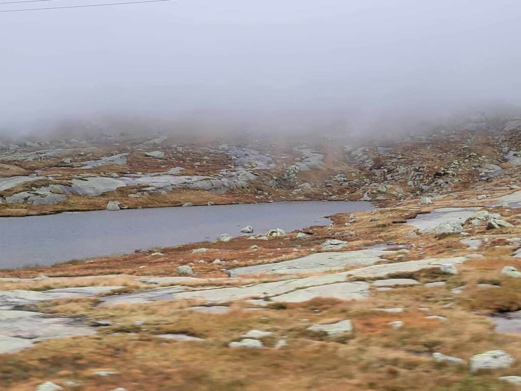 A foggy alpine lake surrounded by rocks, orange moss and grasses