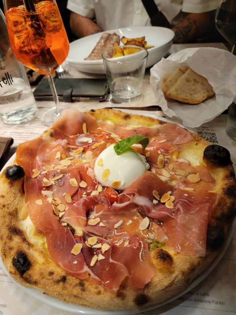 A wood-fired pizza piled with parma ham, shaved almonds, with a whole burrata cheese in the center