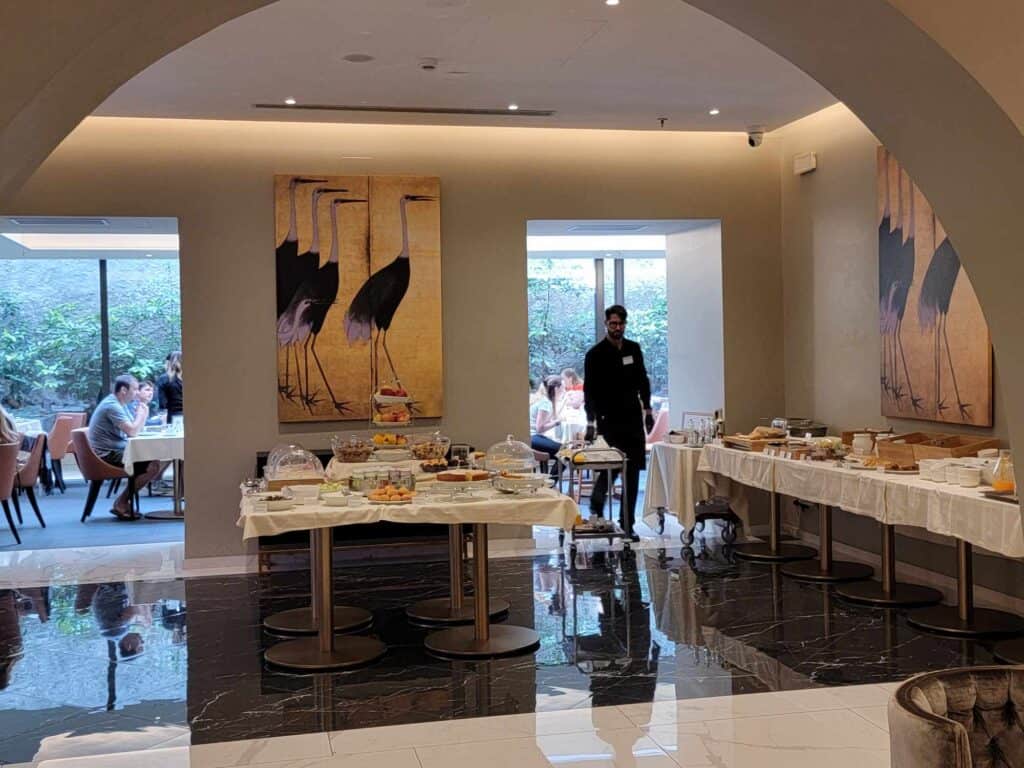 Two large tables spread out with amazing looking baked goods and fruit with a waiter in the doorway to the dining room