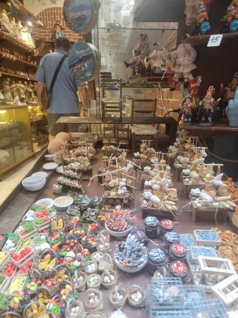 A man browses a shop with tables full of miniature food, and pieces of Nativity scenes