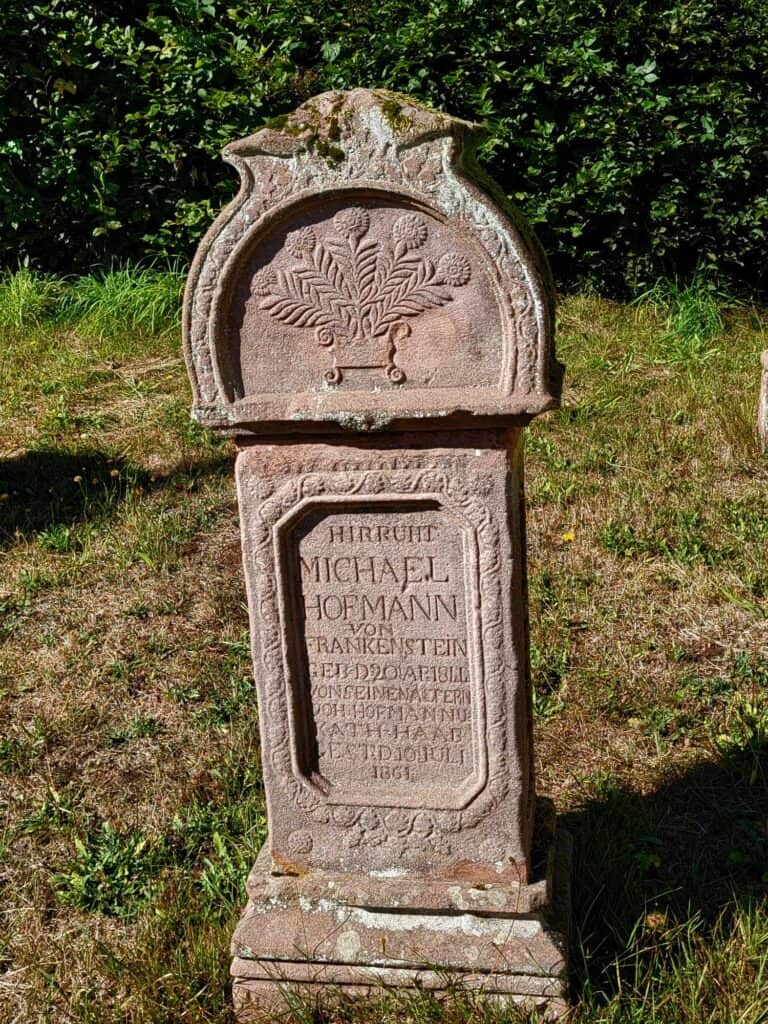 A tombstone of Michael Hoffman von Frankenstein made of red sandstone, rounded at the top with a carved vessel of flowers