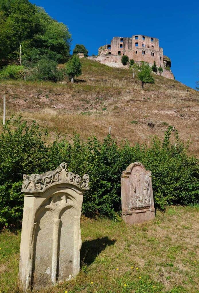 Two very old tombstones, one white limestone, the other red sandstone in the foreground and a large castle ruin on a hill behind to the right