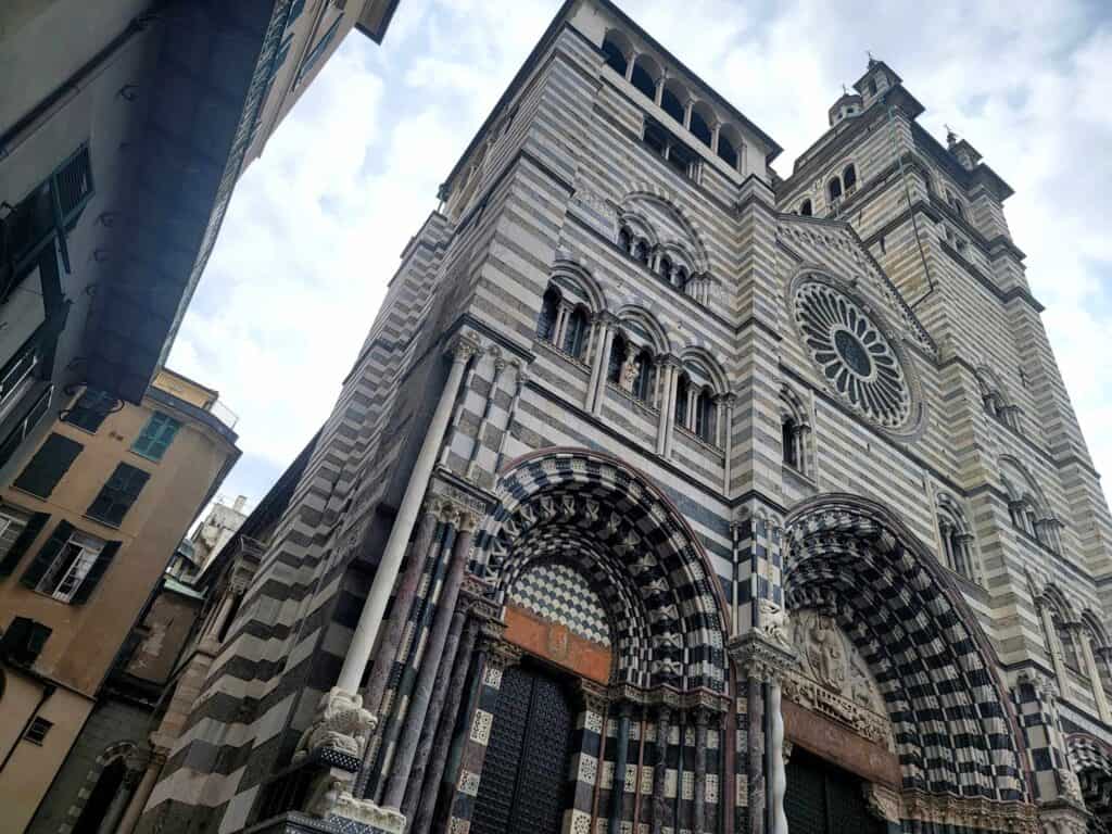 A large stone cathedral with a triple arched doorway, rose window, and stone striped in black and white