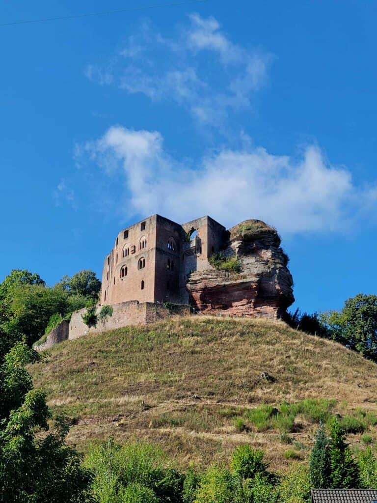 A reddish stone castle ruin on a hill with blue sky and white clouds