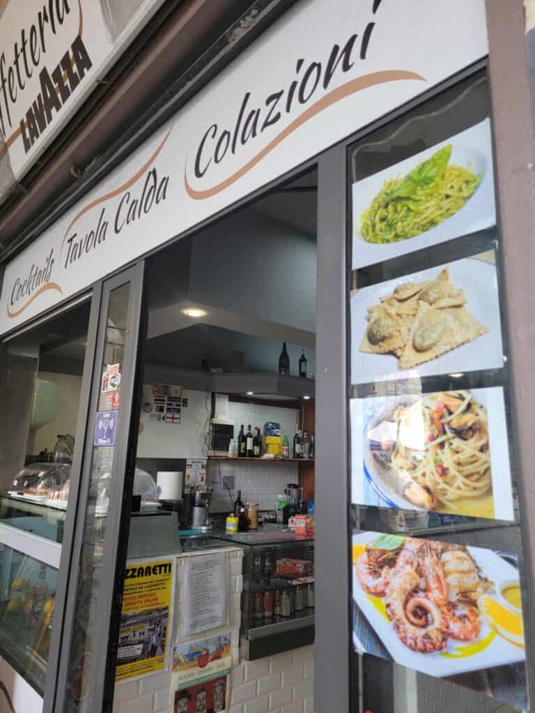 The front of a small eatery displaying photos of pesto pasta, ravioli, and octopus