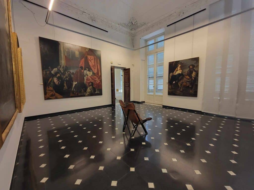 A leather chair in the center of a room with a black and white marble floor aimed at a large Renaissance portrait of a woman that hangs on a white wall