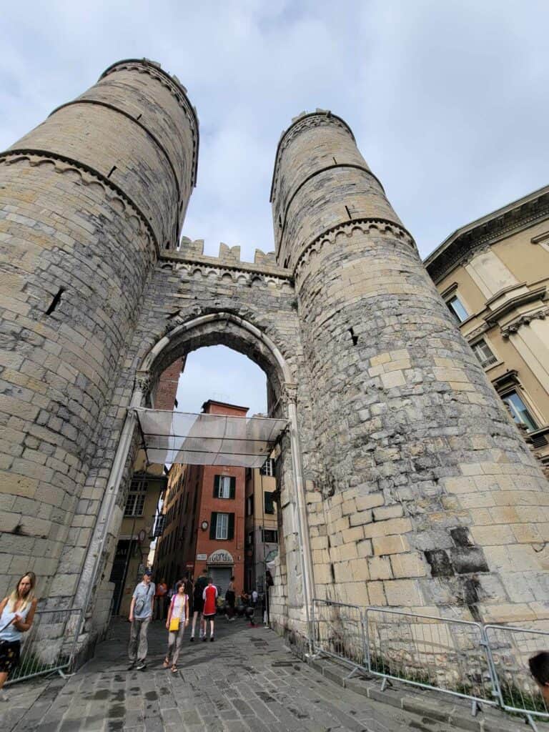 Two large stone towers framing a high arched passageway with people passing through