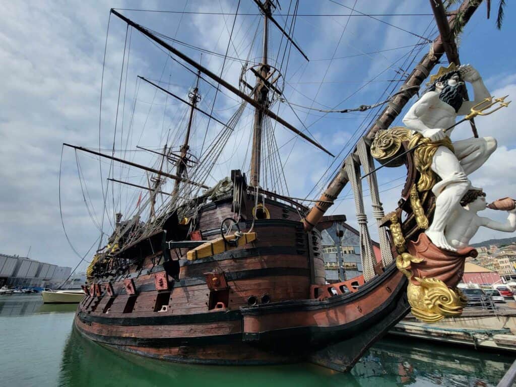 A large, embellished wooden ship in dark tones of wood, with three masts, and a bowsprite of a man with a dark beard