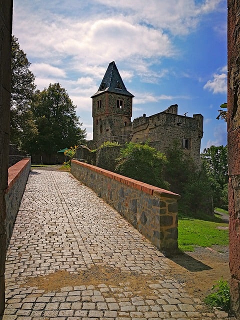 A stone walkway with stone walls on either side and a castle with one pointed turret on the right