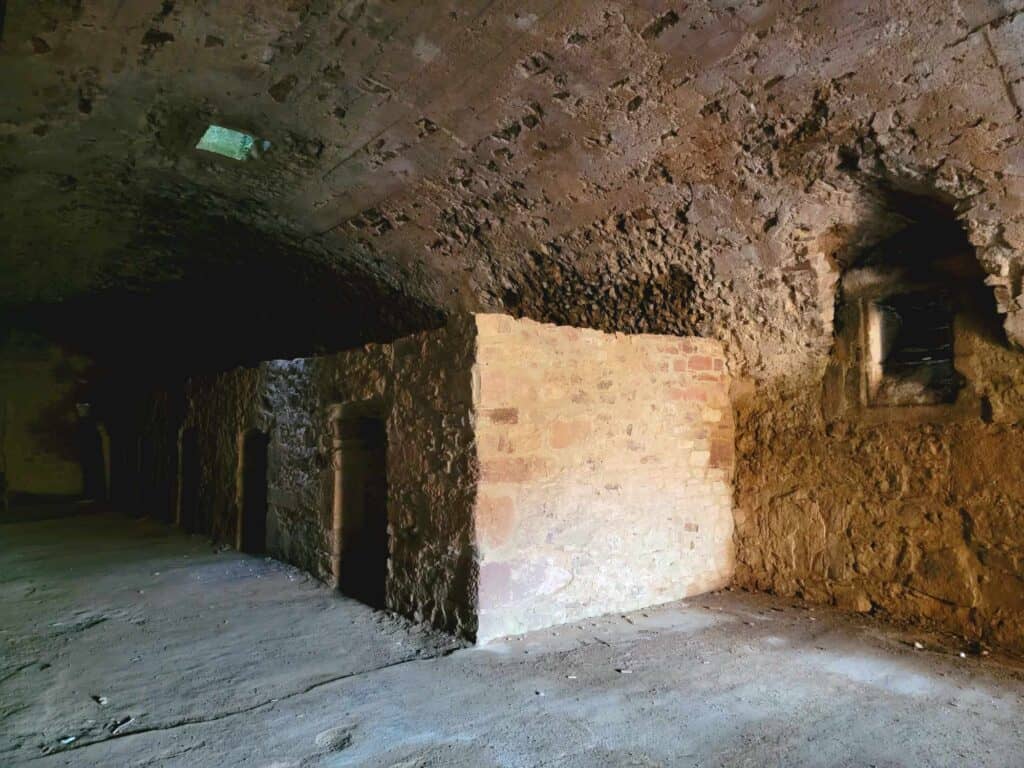 A stone basement with arched ceiling. Inside is a long rectangular structure with multiple small doors on its face