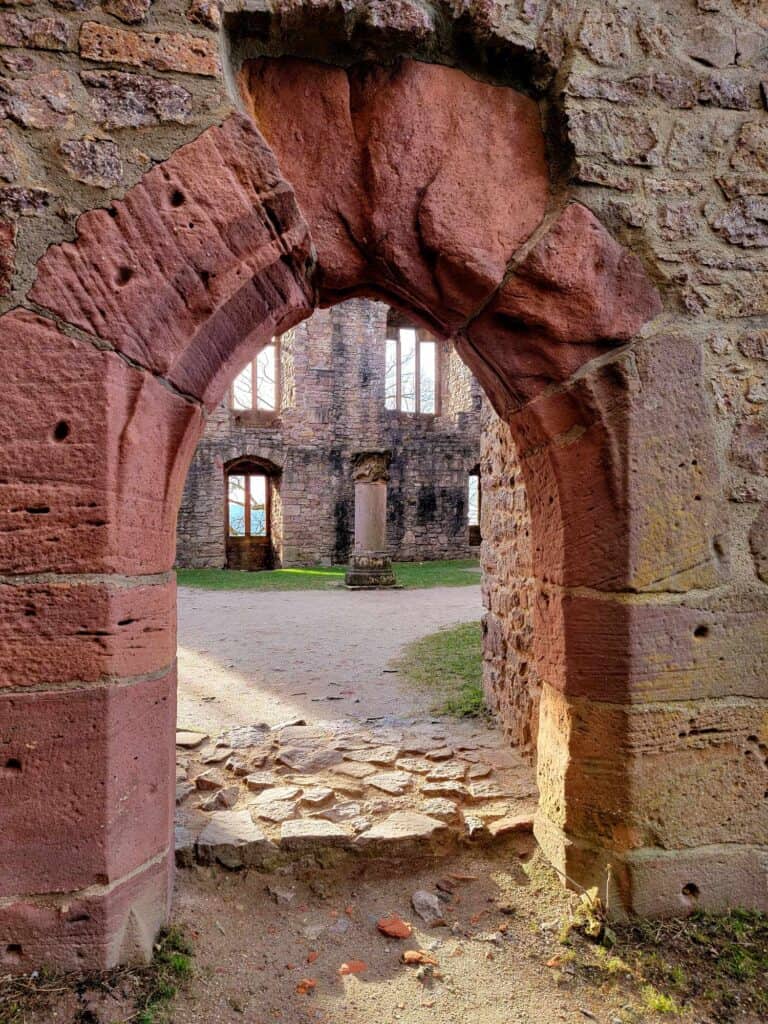 An arched doorway made of reddish sandstone leads to an open courtyard with a truncated column in the center