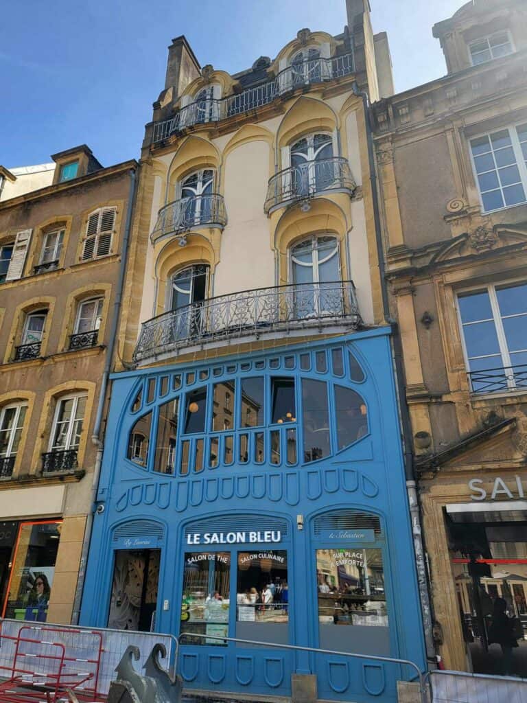 A stunning blue and pale yellow Art Nouveau building with multi-paned rounded windows and a sign Le Salon Bleu