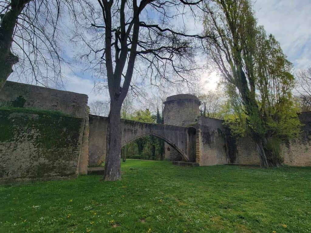 High stone walls with a long low archway under trees