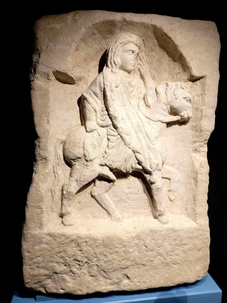 Stone relief of a woman in profile wearing draperies and riding a horse