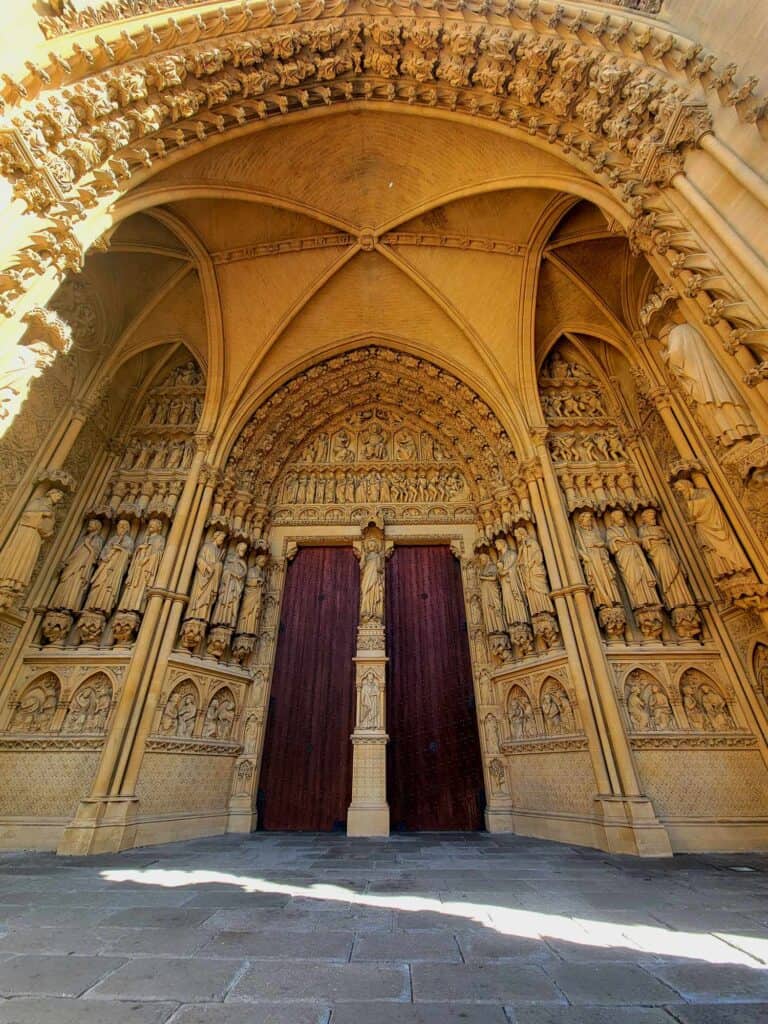 An archway with two wooden doors in the back and dozens of stone statues on either side