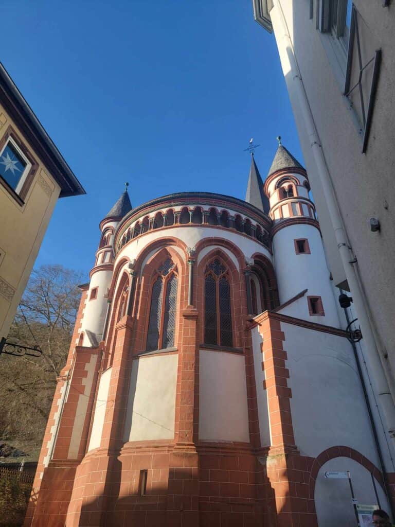 A round chapel from outside a large church. It isi white with red sandstone details and high stained glass windows