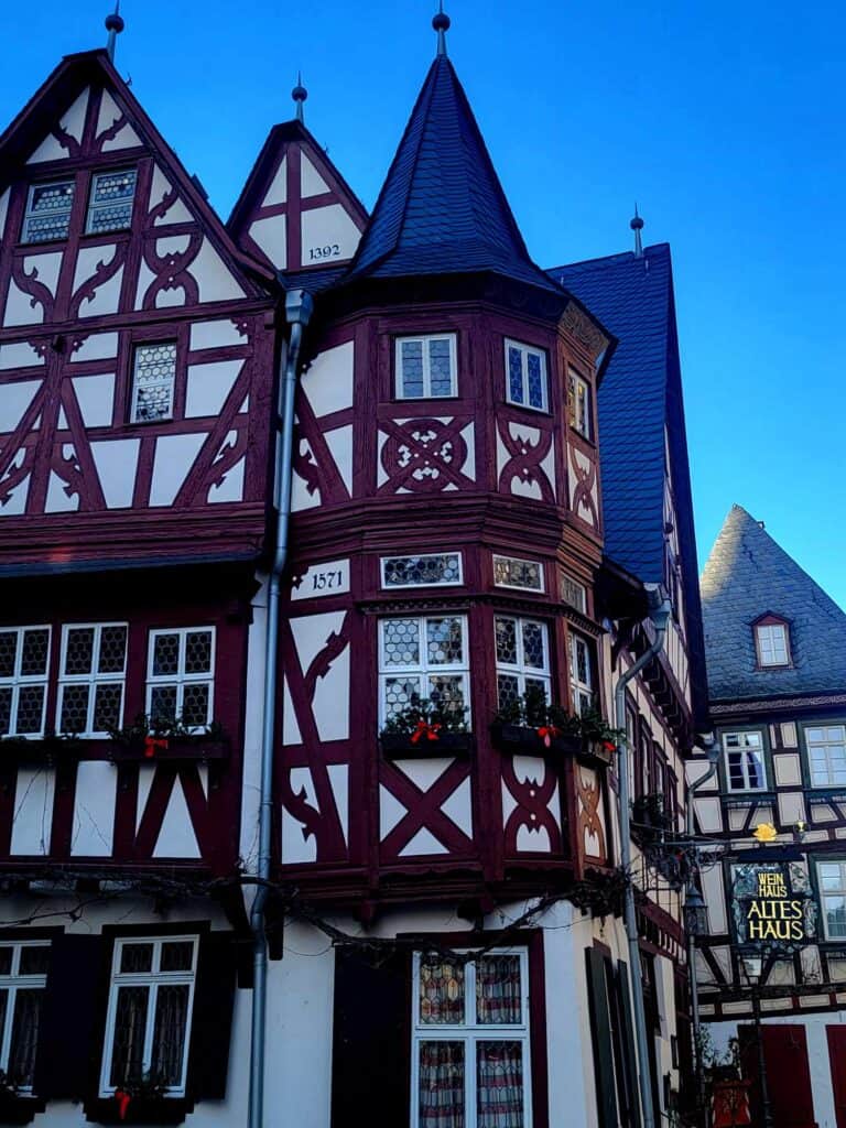 A rounded turret on the corner of a half timbered red and white building with a high pitched roof, and flower boxes