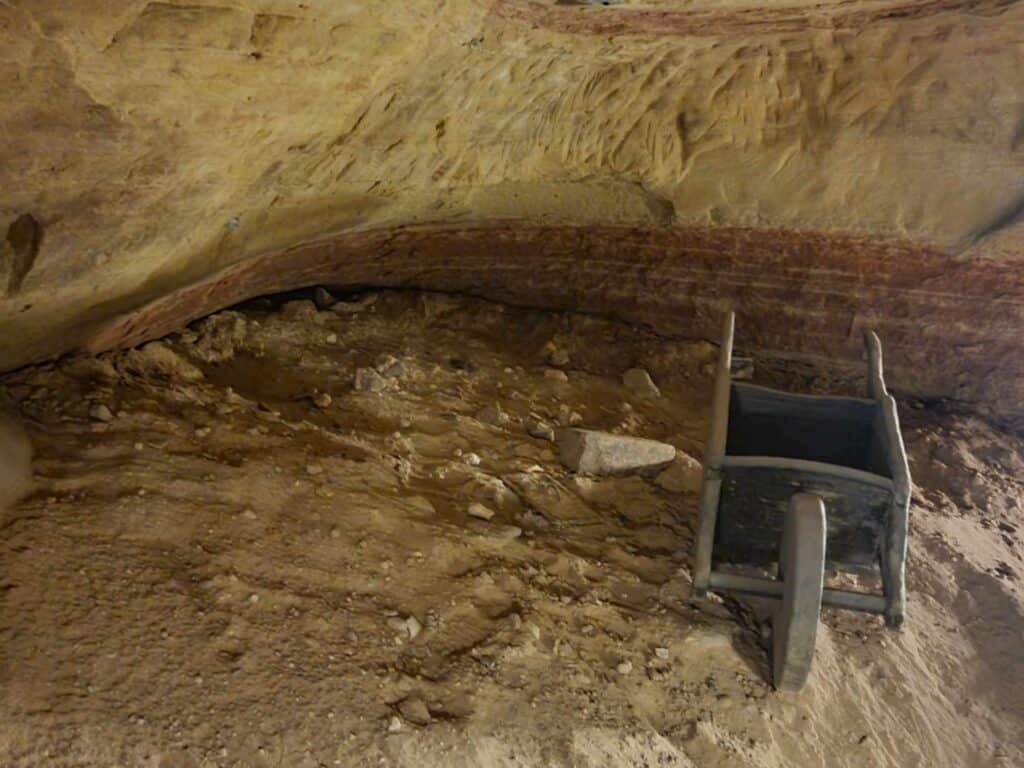 A shallow overhang in a yellow sandstone cave with a small wooden wheelbarrow on the right