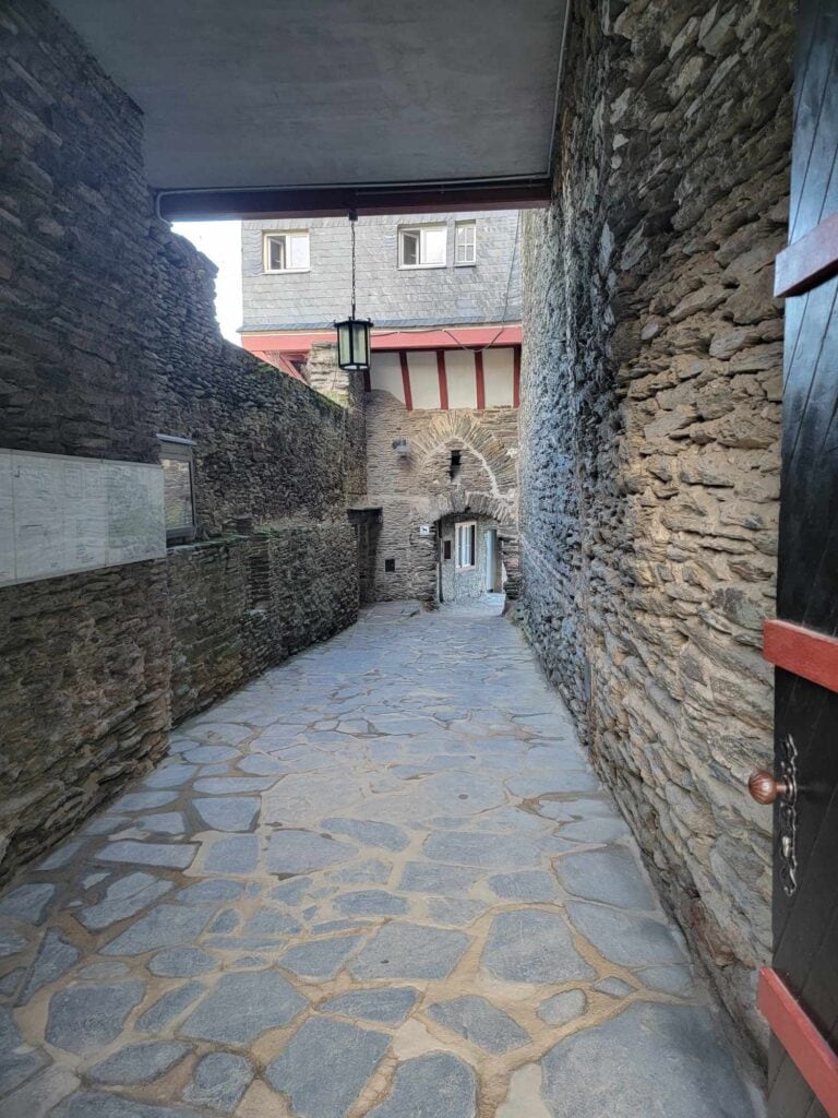 Stone paved passage leading through a doorway with stone walls on either side and an archway at the end