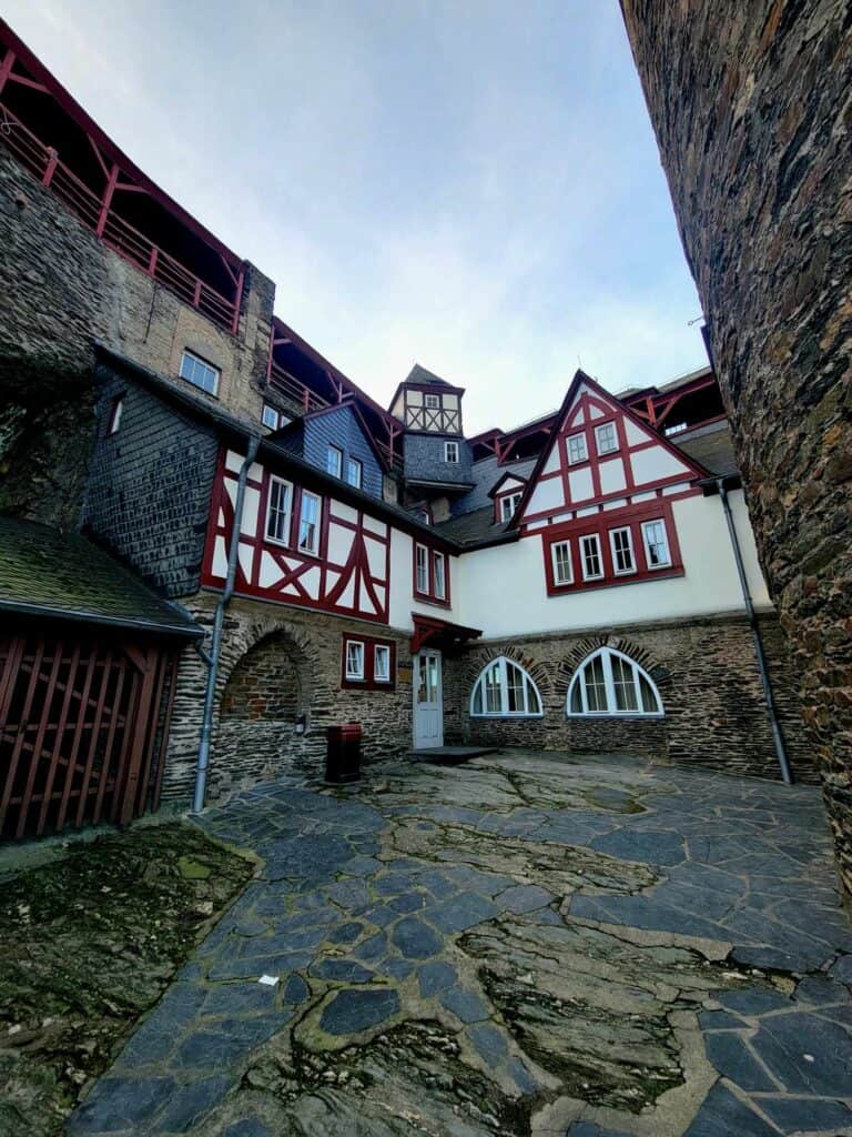 Slate flagstones in an open courtyard flanked by stone walls and a red and white half timbered building