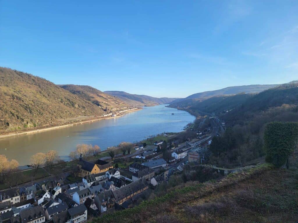 A long blue river winds out of view. Steep vegetated hillside on the left bank and the roofs of a small town on the right.