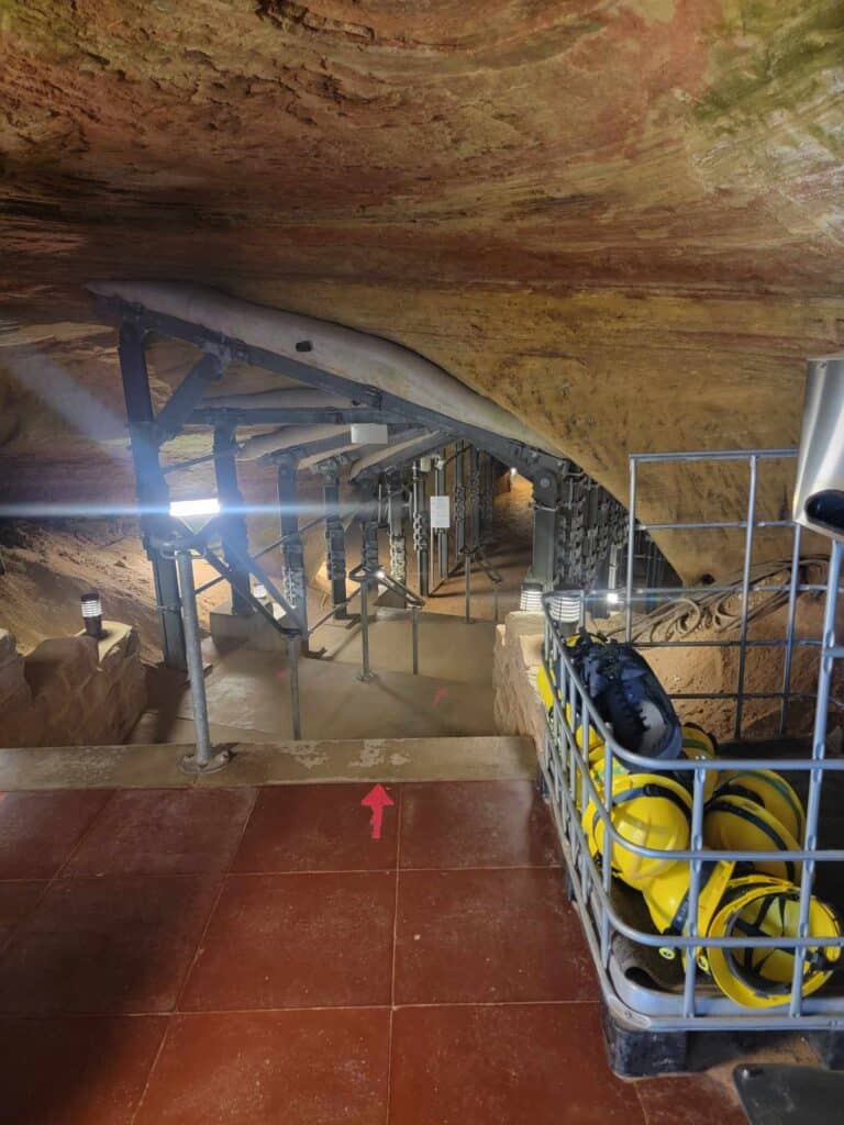 A sandstone cave with a large metal bin full of yellow hard hats on the right