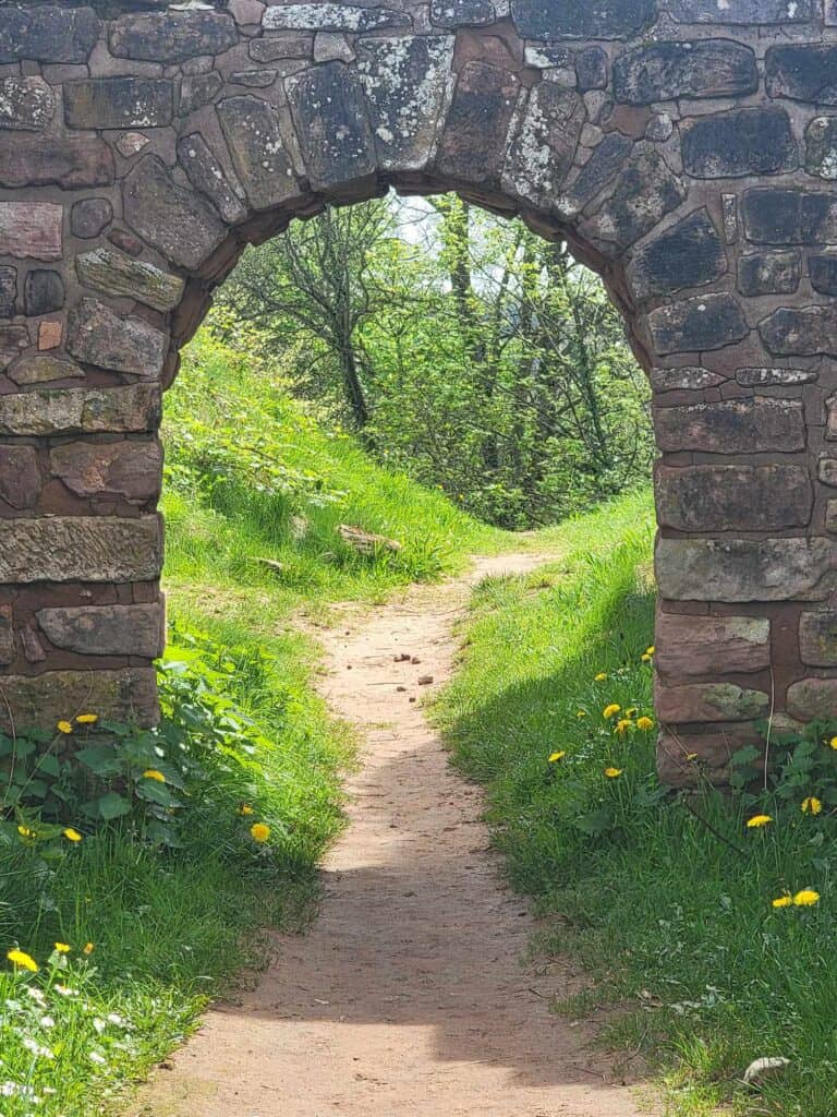 A stone archway with a path leading through to a forest