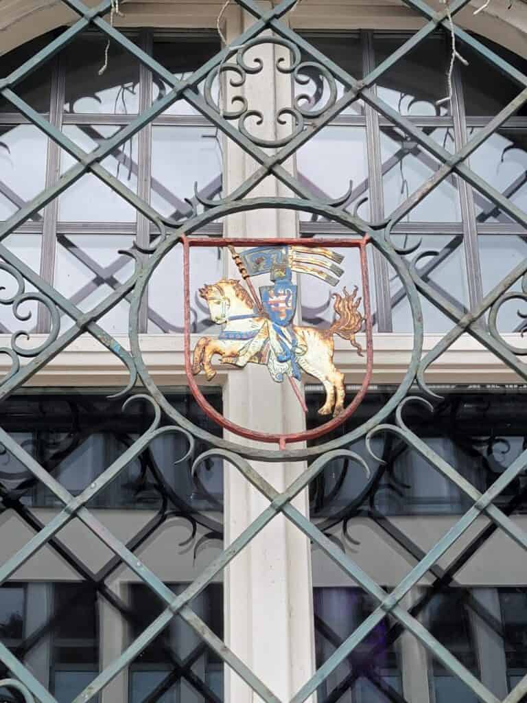 An iron grille with a coat of arms of a knight on a white horse carrying a flag and shield