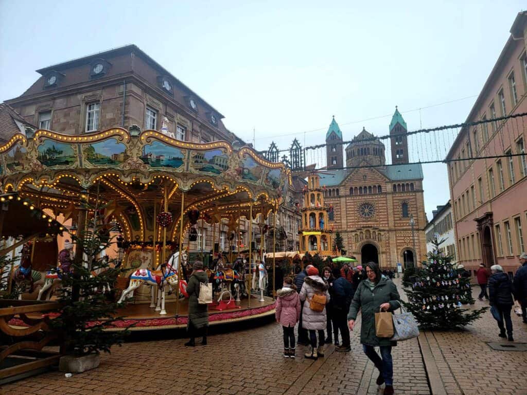 A vintage carousel with horses and children riding with a romanesque cathedral behind