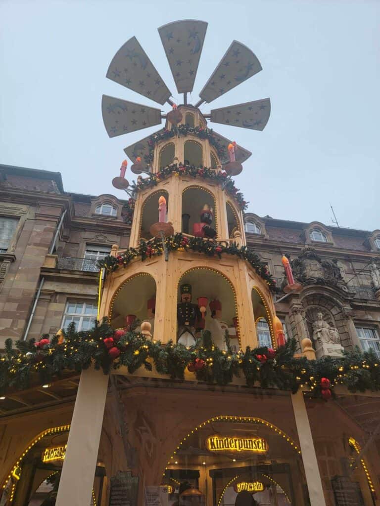 A huge Christmas pyramid with spinning blades on top, arches with wooden figures, and a gluhwein stand on the street level